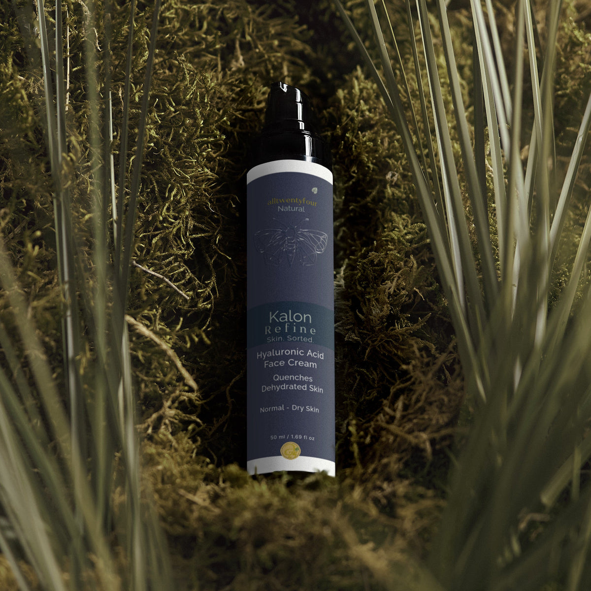 A bottle of Kalon Face Cream placed on a bed of green moss and dried grass blades. The bottle is dark blue with a black spray top and white text.