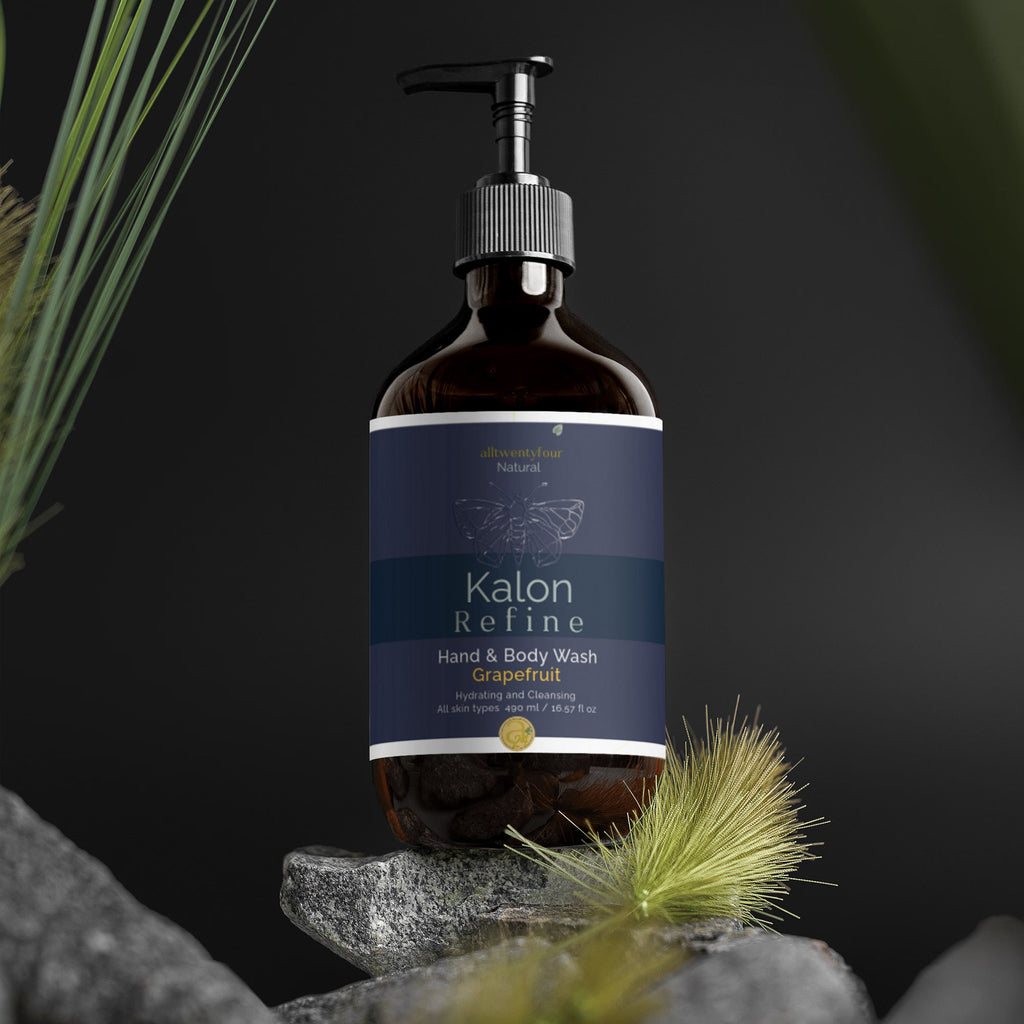 A bottle of Kalon hand and body wash, grapefruit scent, displayed on a stack of gray stones with dried grass against a dark background.